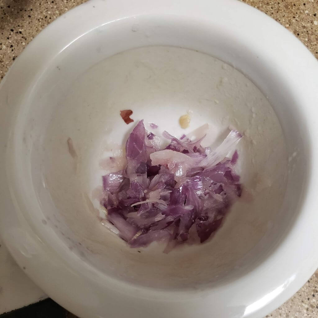 Shallots crushed in mortar and pestle.