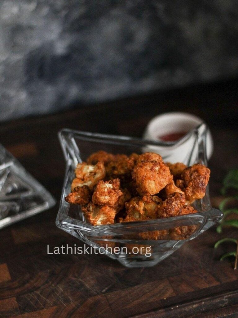 A bowl of cauliflower pepper fry with a bowl of sauce on the side.