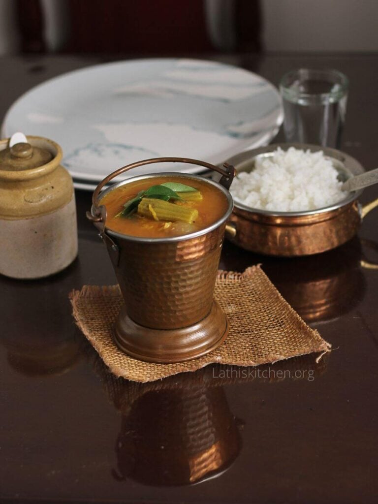 Sambar on a bowl in front of rice bowl and plates.