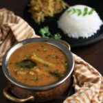 A bowl of sambar in front of a plate with rice and vegetables.