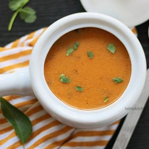 Bowl of tiffin sambar with a spoon on side and cilantro leaves.