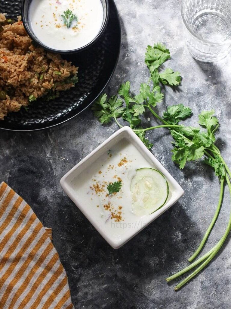Top view of cucumber raita with a plate of biryani.