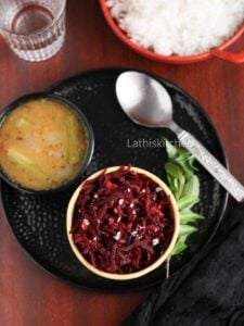 Over head shot of a plate with beetroot stir fry in a bowl, sambar, a spoon and a sprig of curry leaves.