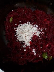 Grated coconut added to the cooked beetroot in a pan.