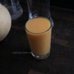 A glass of cantaloupe smoothie with two empty glasses on the background.