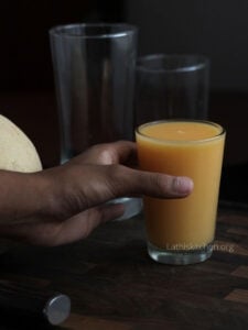 A hand holding a glass of cantaloupe smoothie.