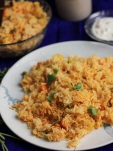 Close up of vegetable biryani in a plate with bowl of rice in out of focus.