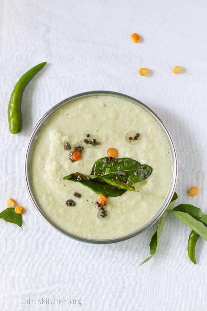 Top view of coconut chutney with roasted gram dal green chili and curry leaves on side.