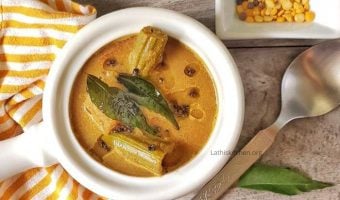 Bowl of Kerala Varutharacha sambar with a spoon, curry leaf and pepper on side.
