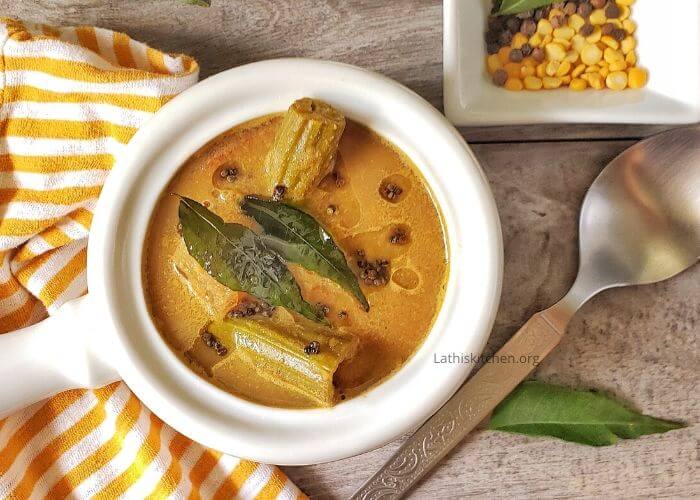Bowl of Kerala Varutharacha sambar with a spoon, curry leaf and pepper on side.