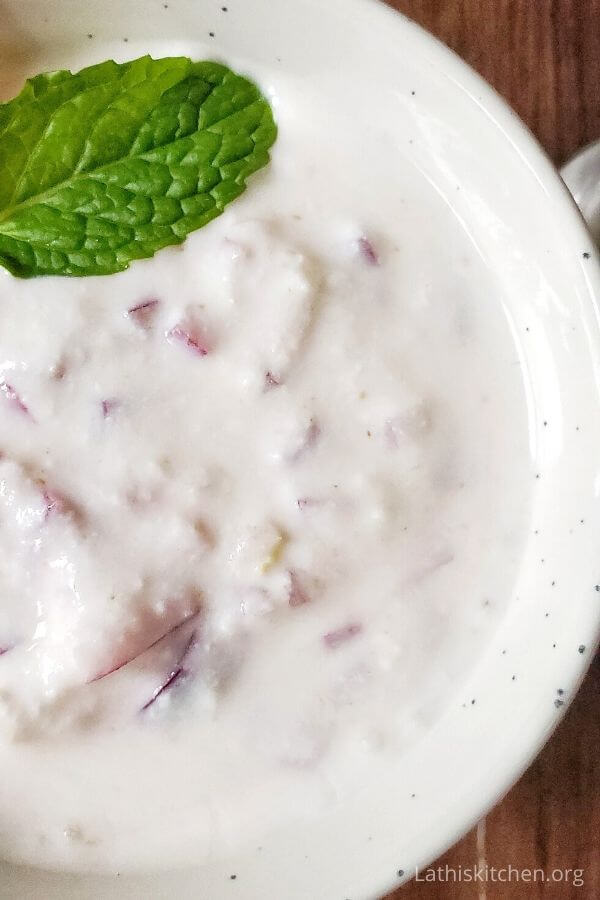 Picture of half bowl with onion raita and a mint leaf.