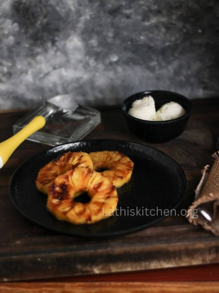 Grilled pineapples on a plate with scoops of ice cream in a bowl behind.