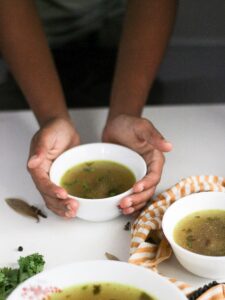 Hands holding a bowl of chicken soup.