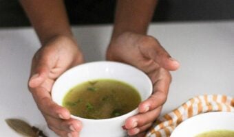 Hands holding a bowl of chicken soup.