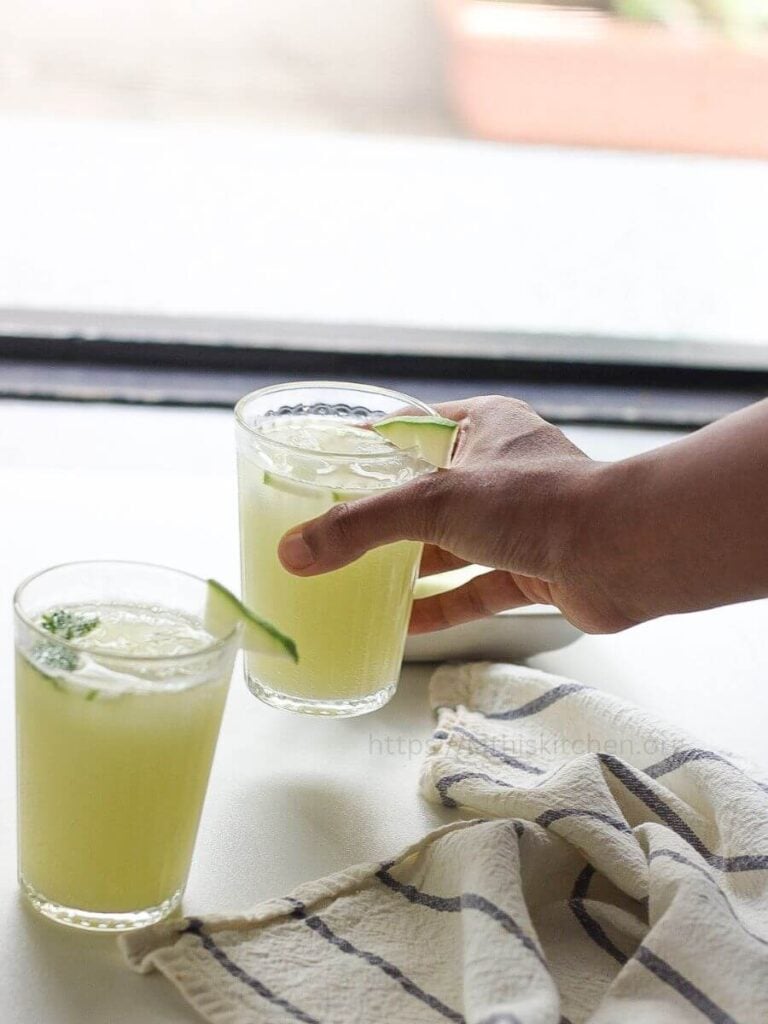 A hand picking up a glass of raw mango ginger cooler.