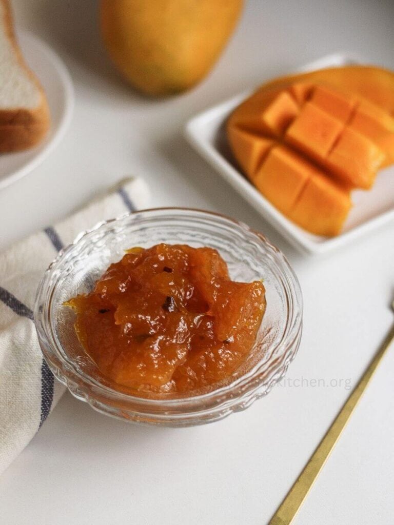 A bowl of mango jam with mango slices on a plate in the side.