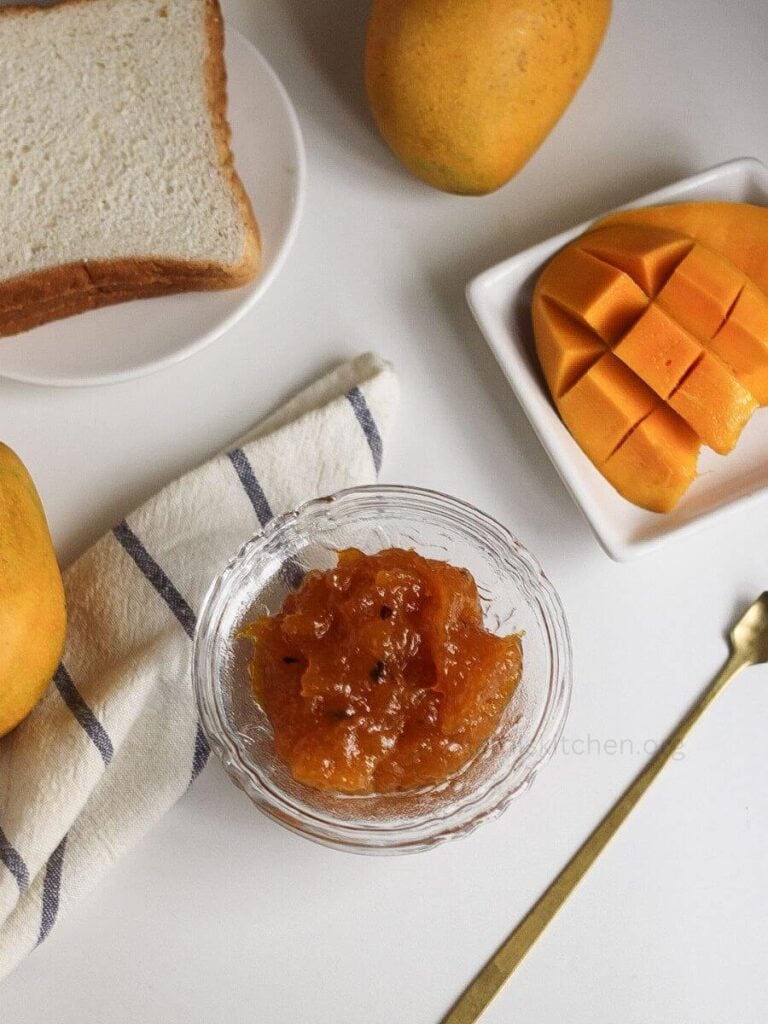 A bowl of Instant Pot mango jam with bread slices and mango pieces on the side.