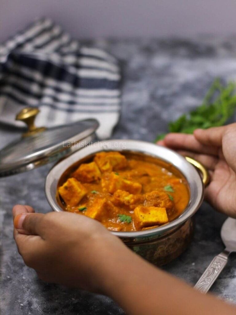 A hand picking a bowl of restaurant style paneer butter masala.