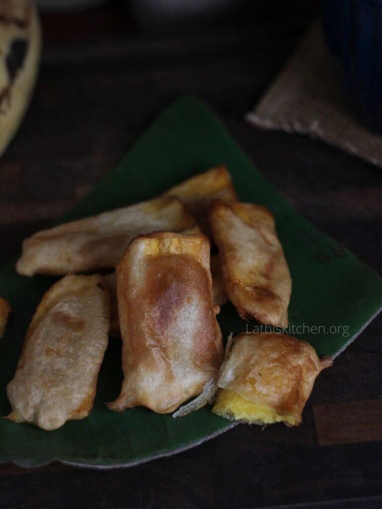 Banana fritters stacked on a banana leaf.