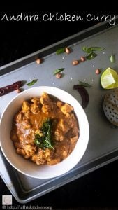 Bowl of Andhra Chicken Curry with peanut, red chilies and lemon wedge on side.