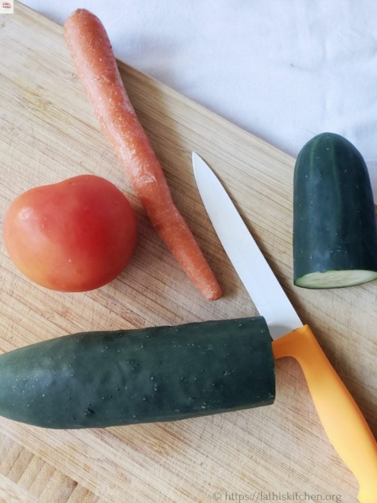 Carrot, cucumber and tomato on the chopping board with a knife.