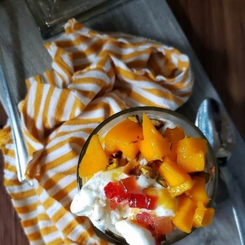 Glass of Mango Milkshake with Ice cream, nuts and mango chunks.