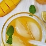 Glass of Mango Lemonade with Mango and lemon wedges on side.