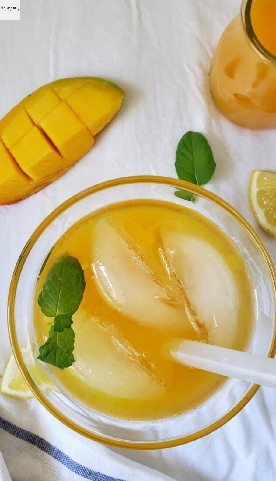 Glass of Mango Lemonade with mango and lemon wedges on side and mint leaves.