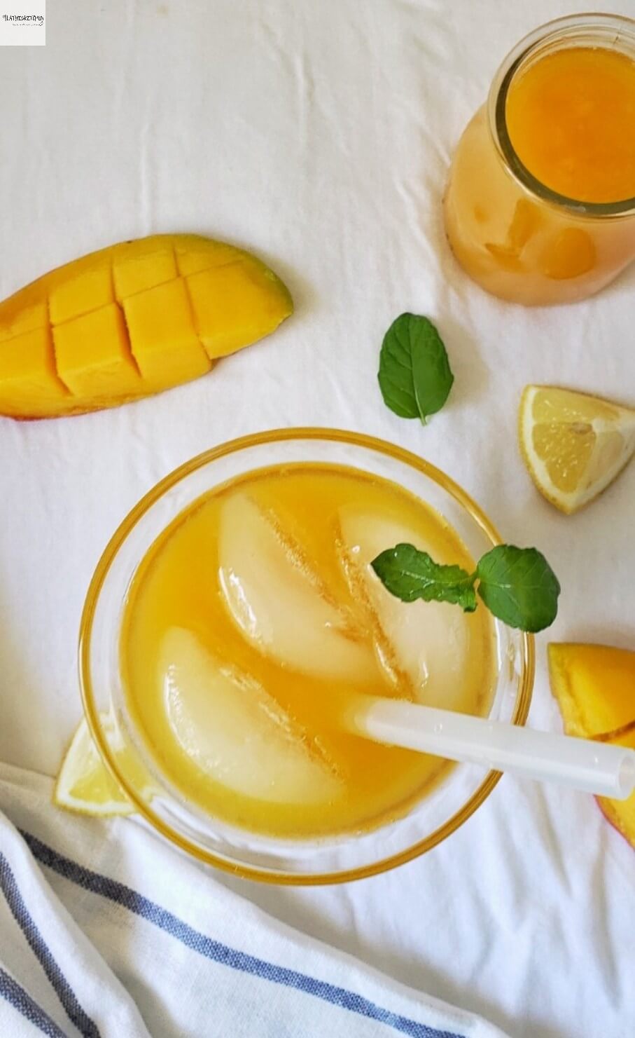 Glass of Mango Lemonade with mango and lemon wedges on side and mint leaves.