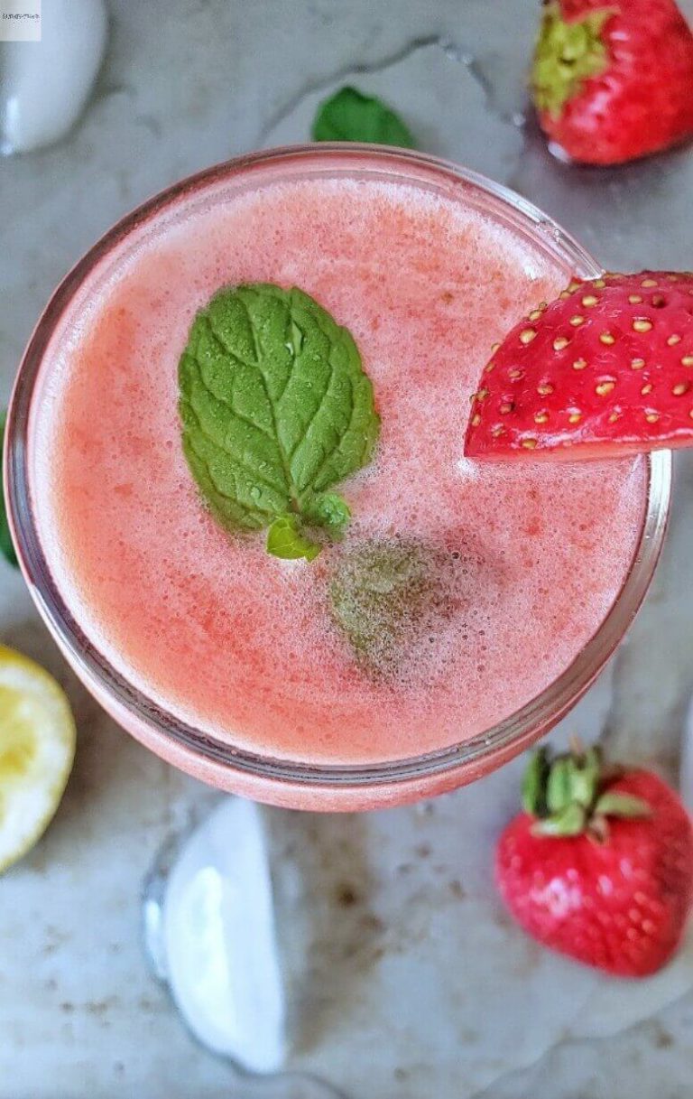 Glass of Strawberry Lemonade with mint leaf on it and fresh strawberries below.