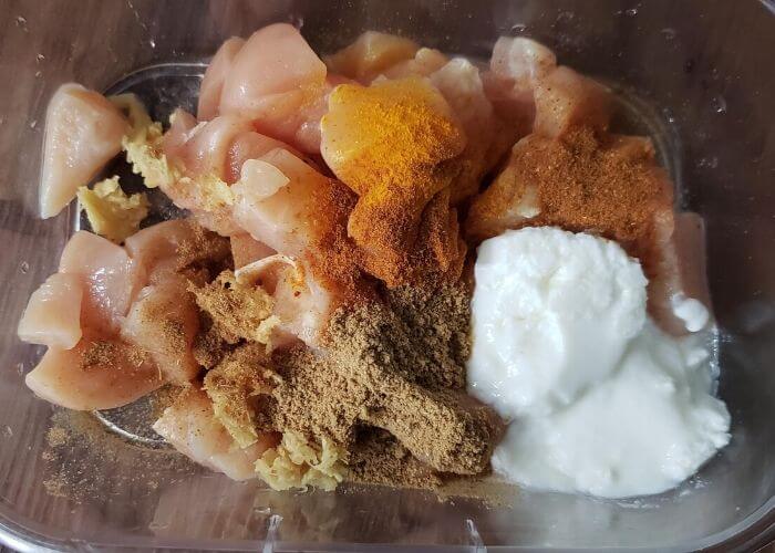 Chicken marinating with yogurt and spices in a bowl.
