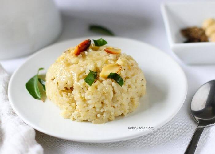 a plate of ven pongal with nuts and curry leaves.