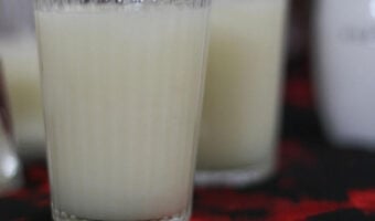 A glass of cucumber fruit smoothie with two glasses in out of focus behind.