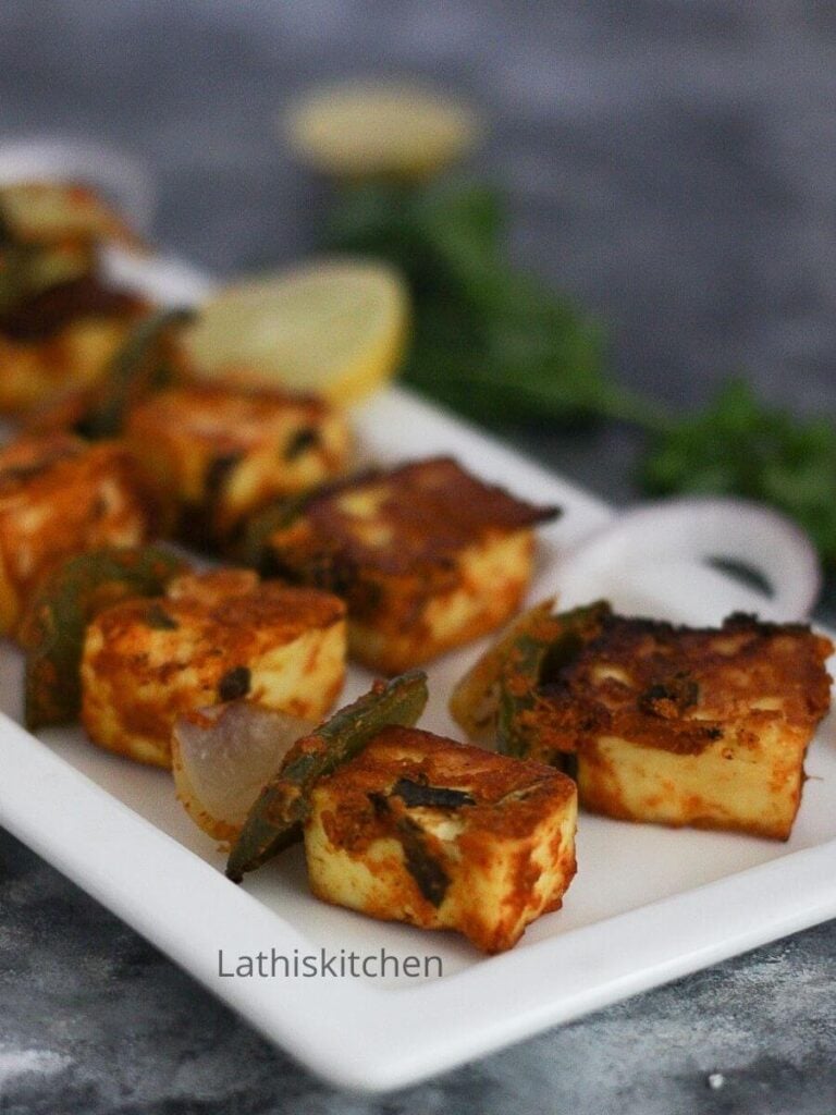 Plate with paneer tikka arranged with lemon wedge and onion.
