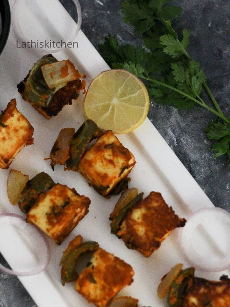 Baked paneer tikka on the plate with lemon slice and onion rings.
