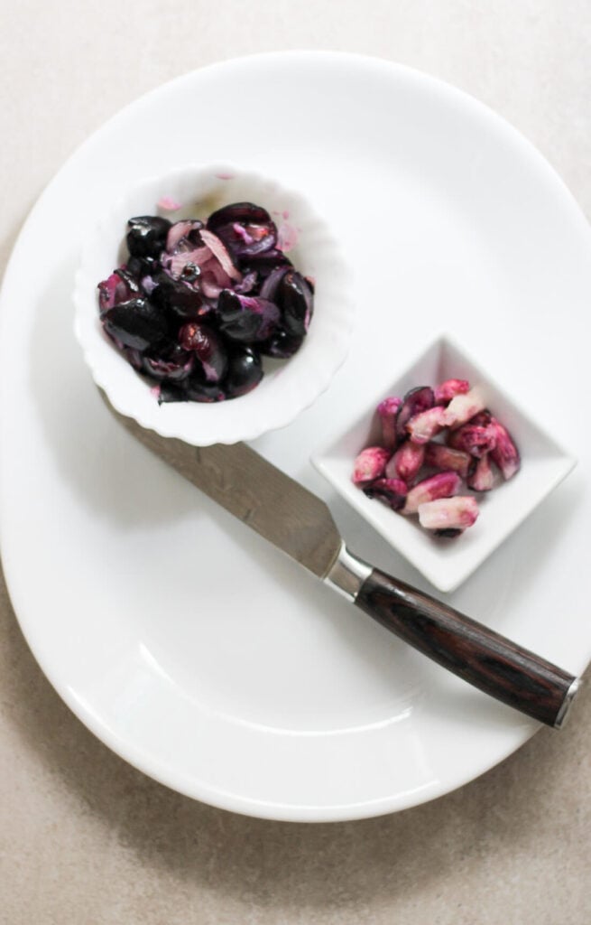 Deseeded black plums in a bowl with seeds in another bowl.