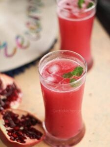 Pomegranate mocktail in two glasses with cut open pomegranate fruit on side.