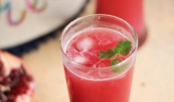 Pomegranate mocktail in two glasses with cut open pomegranate fruit on side.