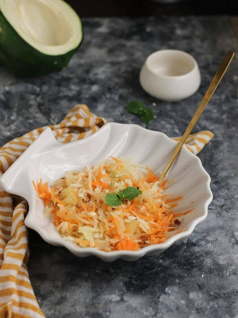 A bowl with green papaya salad with a mint leaf on top.